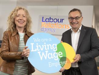 A man and woman holding a sign with the text "We are a living wage employer" in front of the Labour Relations agency logo.